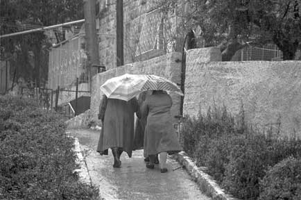 Drei
                Frauen auf einem Fussweg im Regen mit Schirmen